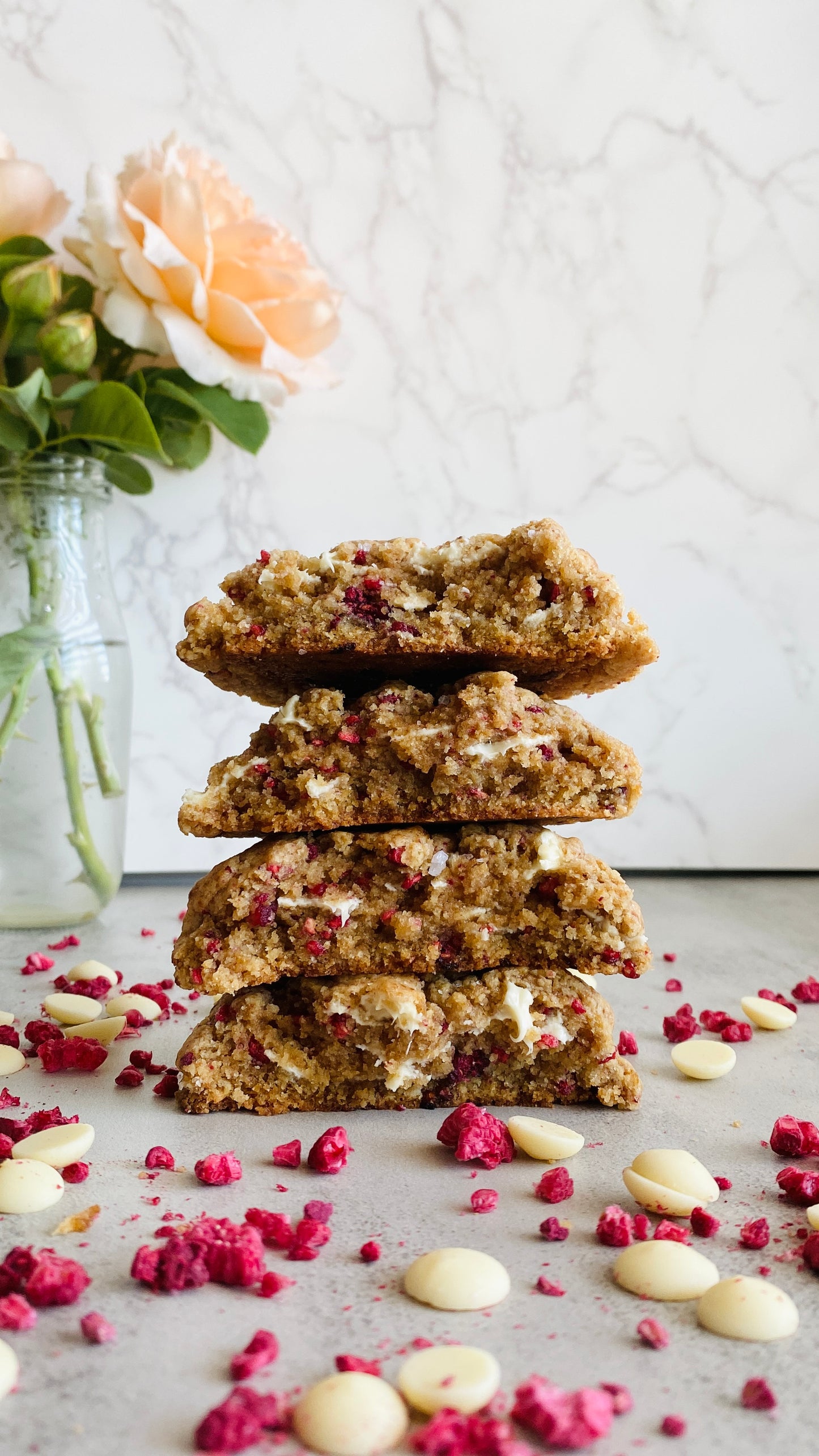Stack of cookies with white chocolate chips and pink freeze-dried raspberries on a light surface.