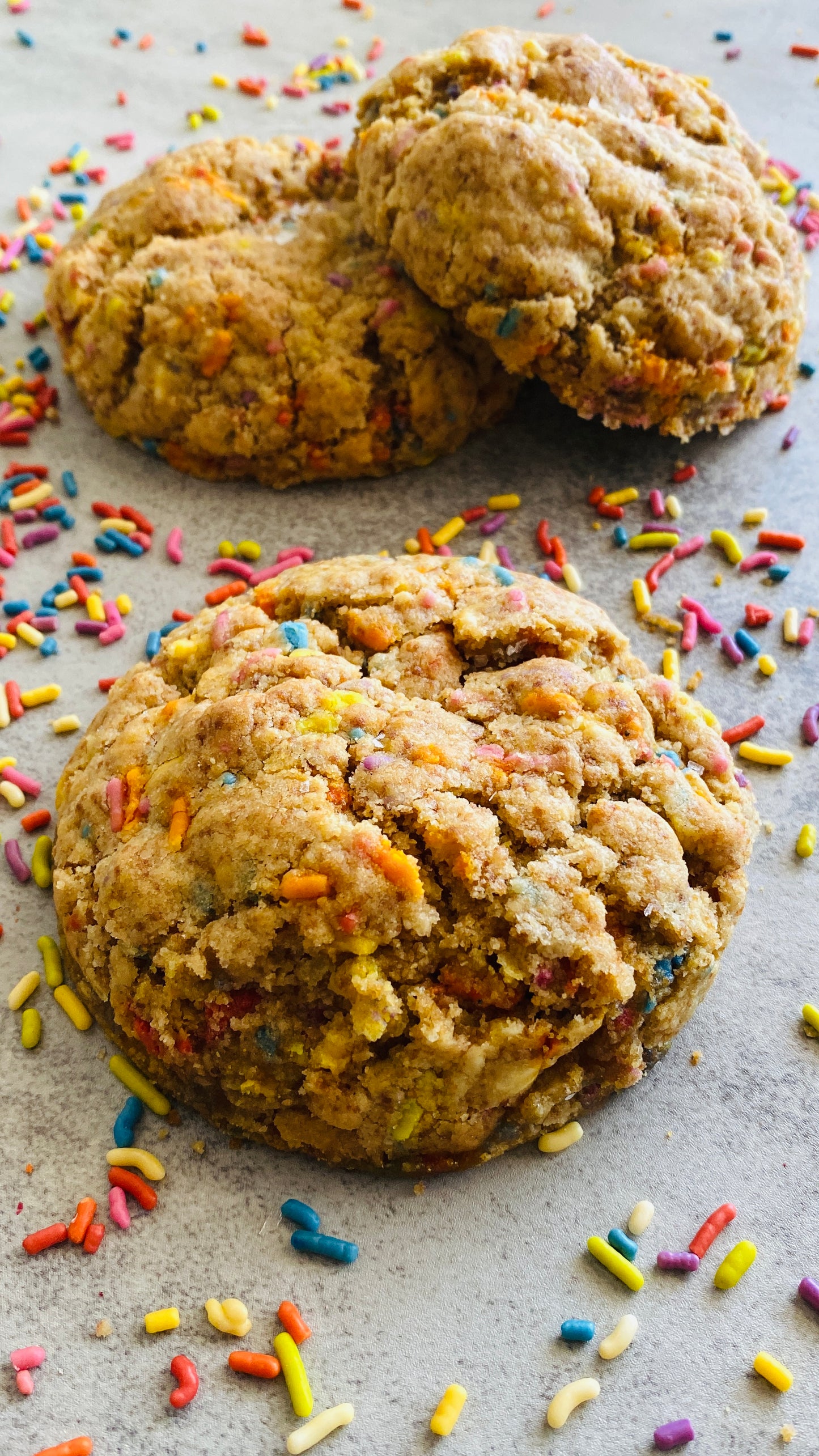 Three cookies with colorful sprinkles on a gray surface