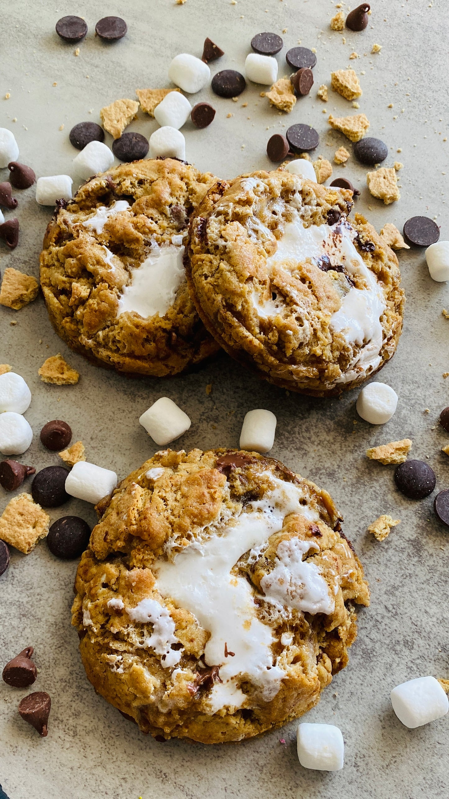 Cookies with marshmallows, chocolate chips, and graham cracker pieces on a stone surface