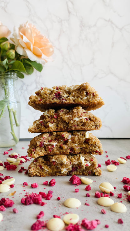 Stack of cookies with white chocolate chips and pink freeze-dried raspberries on a light surface.