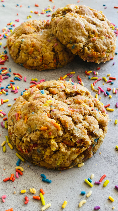 Three cookies with colorful sprinkles on a gray surface