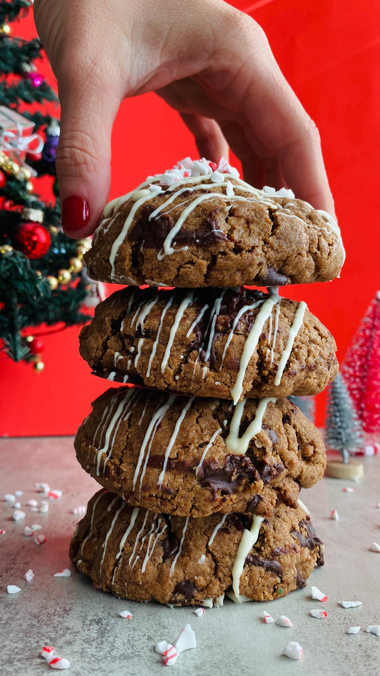 Stack of cookies with a hand reaching for the top one against a red background with Christmas trees.