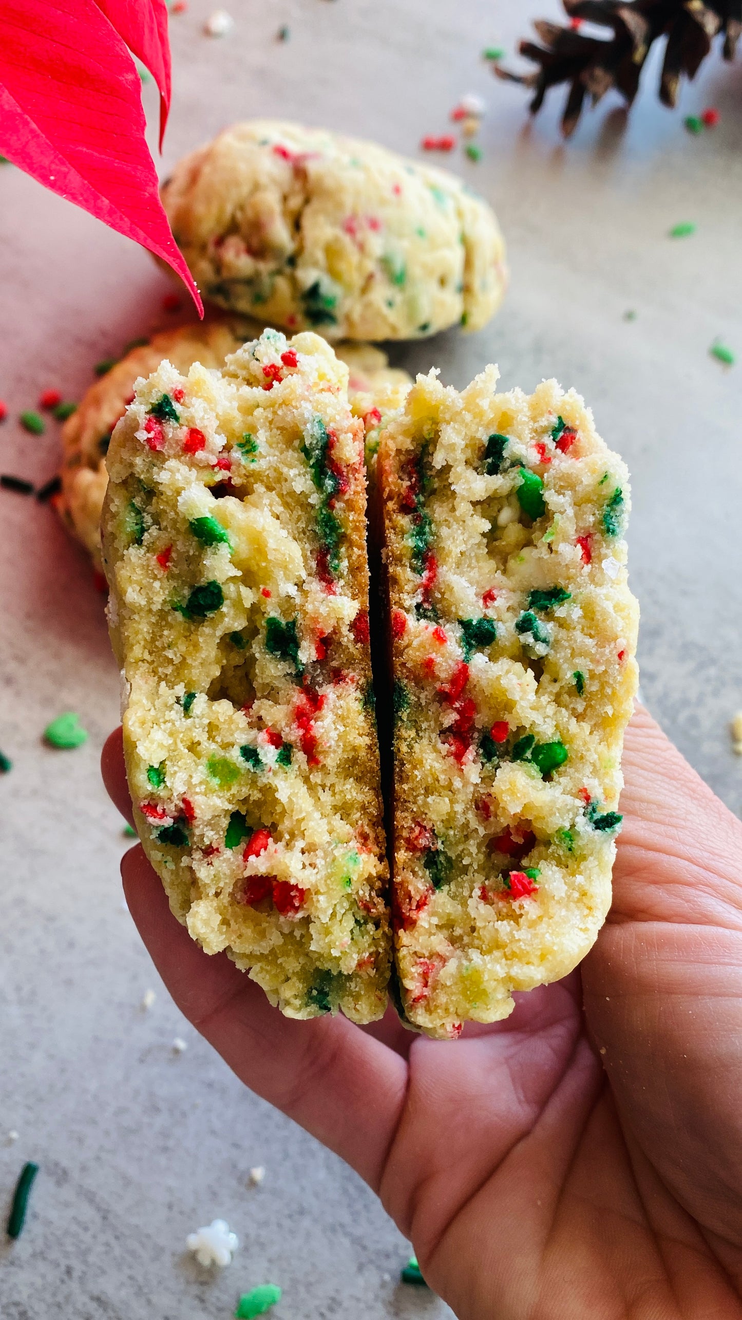 Hand holding a split cookie with colorful crumbly interior on a light background