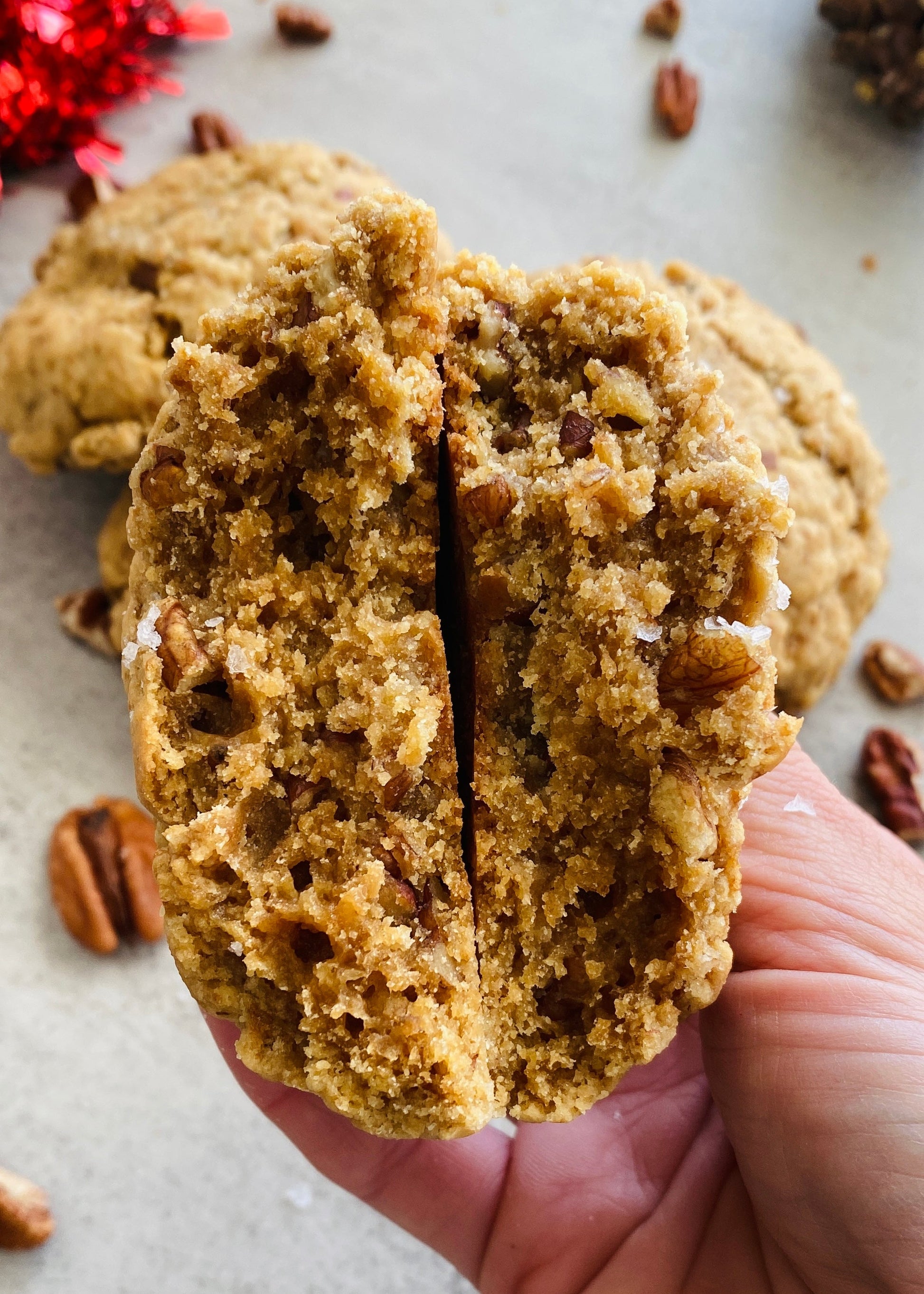Hand holding a cookie with pecans on a light surface